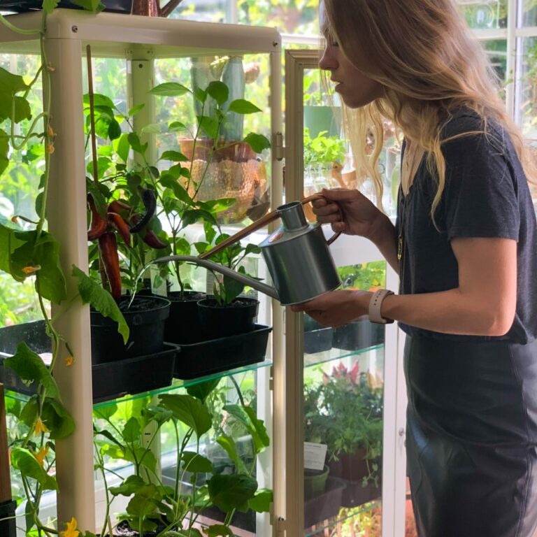 Woman waters her plants which are in pots on a shelf.
